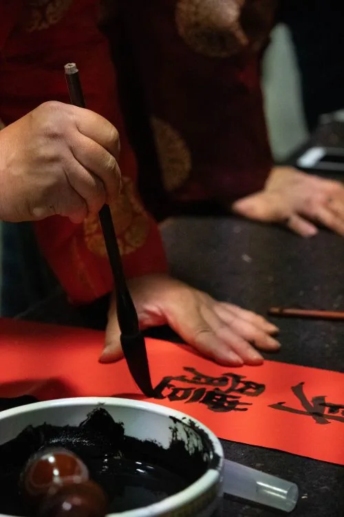 毛笔在红纸上书写汉字的手部局部（课程示意图，非机构现场）